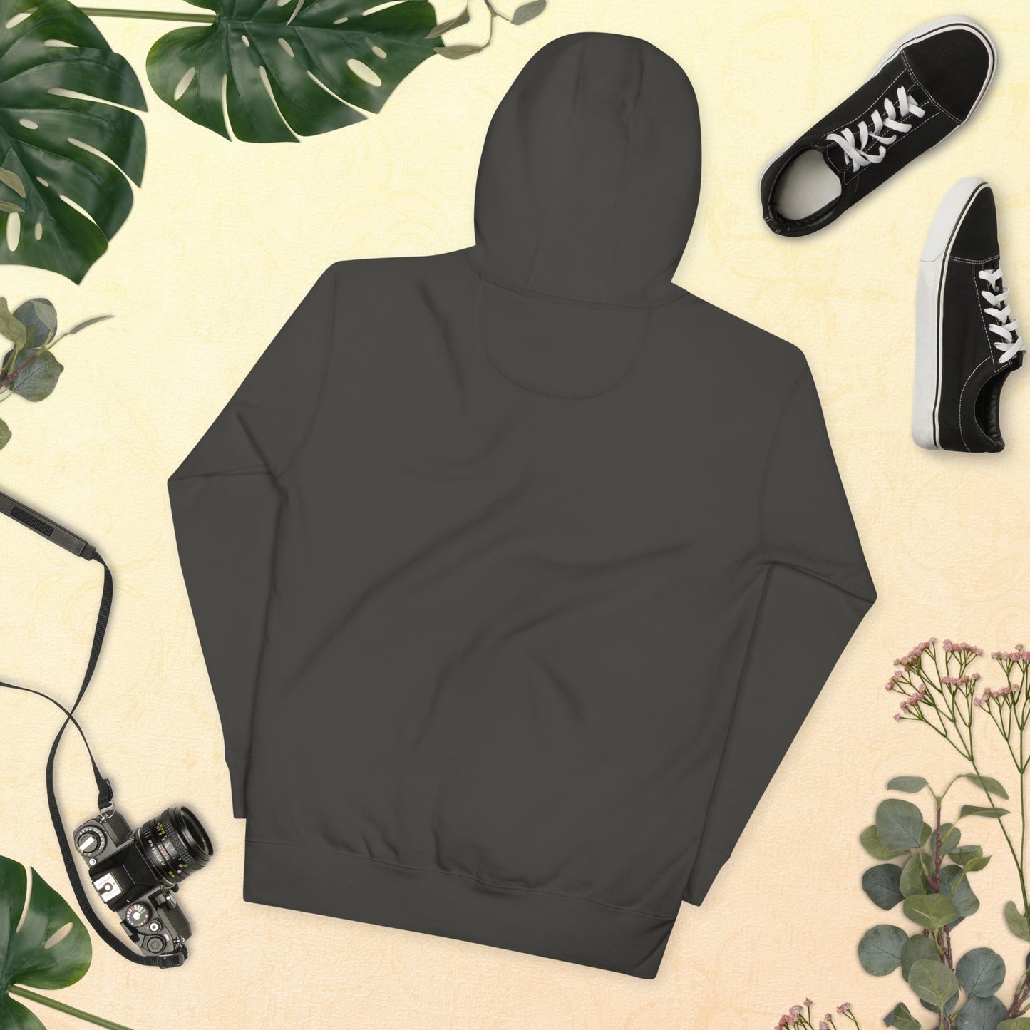 Dark gray hoodie on a beige background with plants and black sneakers.