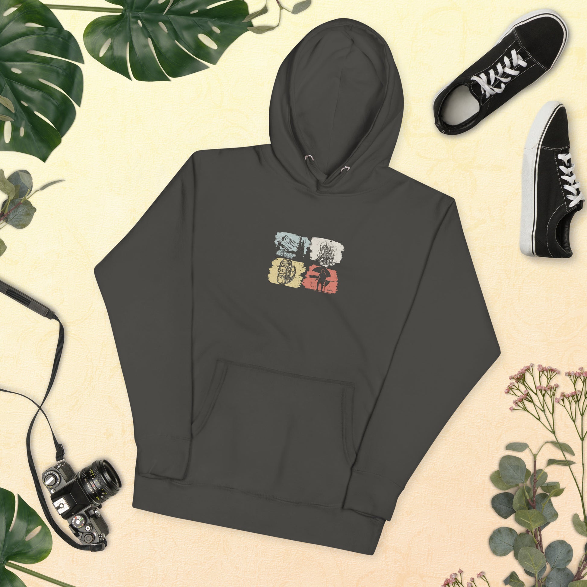Dark grey hoodie with camping and equipment graphics on a beige background with plants and shoes.