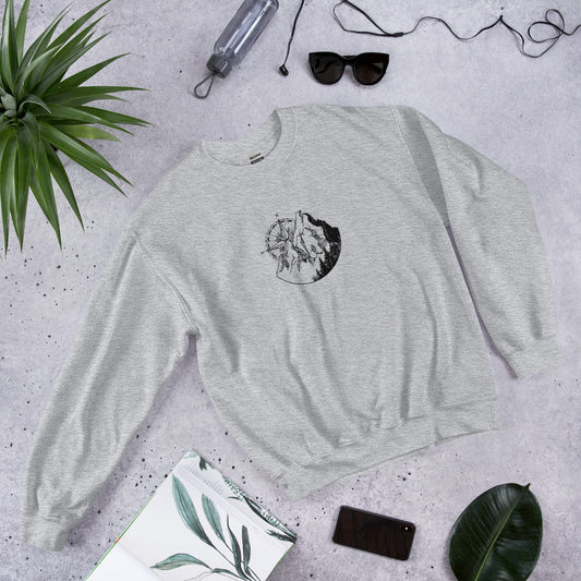 Grey t-shirt with Mountain Compass graphic design on concrete surface with plants and accessories.