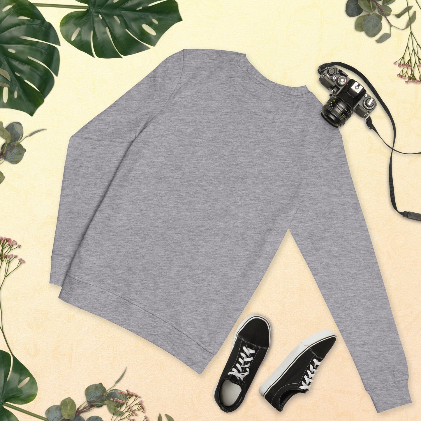 Gray long-sleeve shirt with black sneakers and a camera on a light background with green leaves.