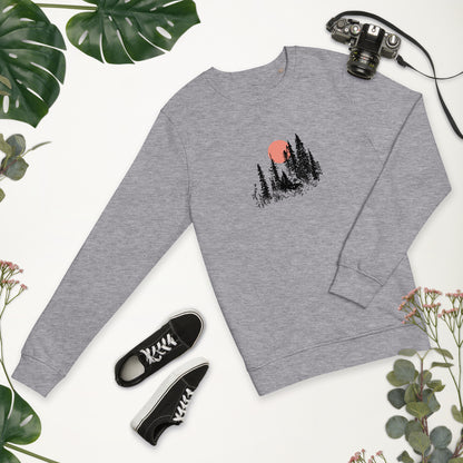 Gray sweatshirt with nature forest graphic, black sneakers, and camera on a white background with greenery.