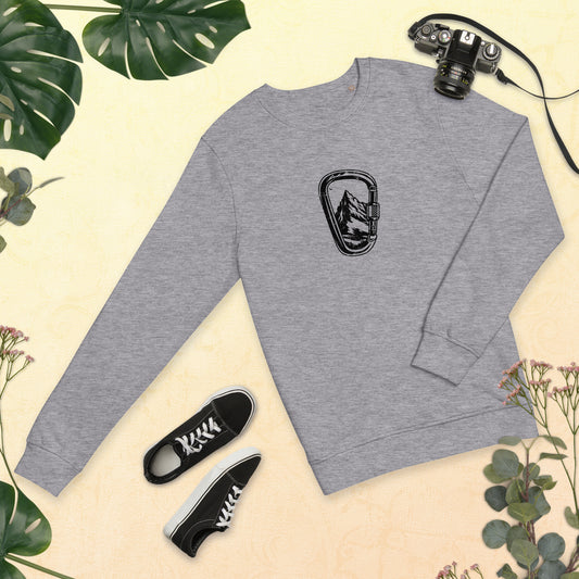 Gray t-shirt with Carabiner Mountain Black design, black sneakers and camera on beige background with green leaves.
