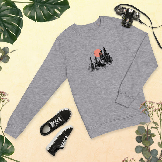 Gray sweatshirt with nature-themed forest design, black sneakers, and camera on a beige background with greenery.