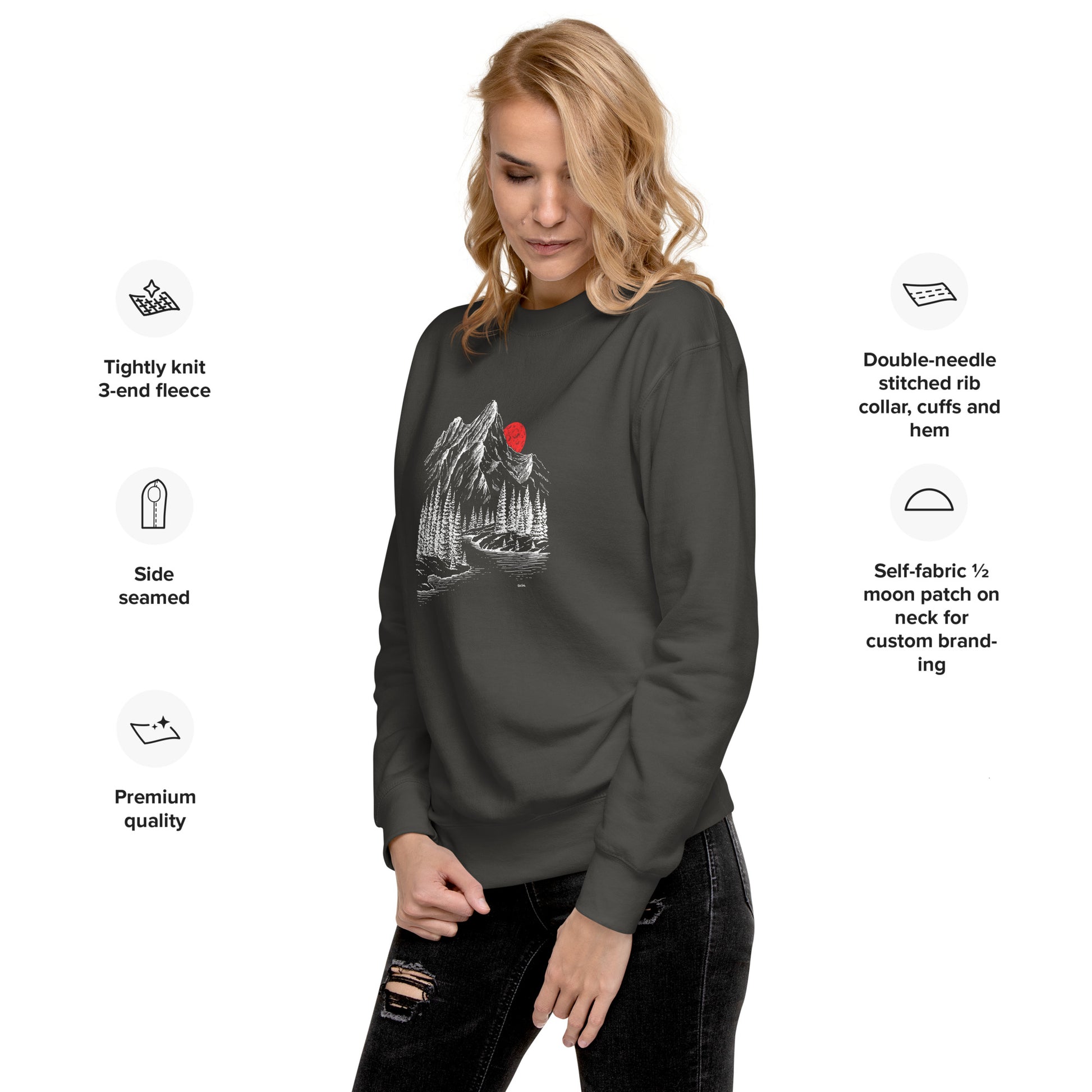 Woman wearing a dark gray sweatshirt with a graphic design mountain sketch forest on a white background, featuring text about sweatshirt features.