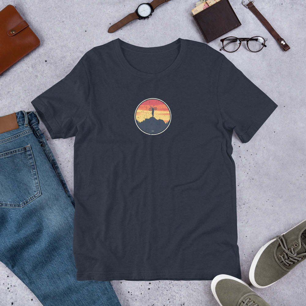 Black t-shirt with mountain bike graphic design on grey surface with jeans, shoes and accessories.