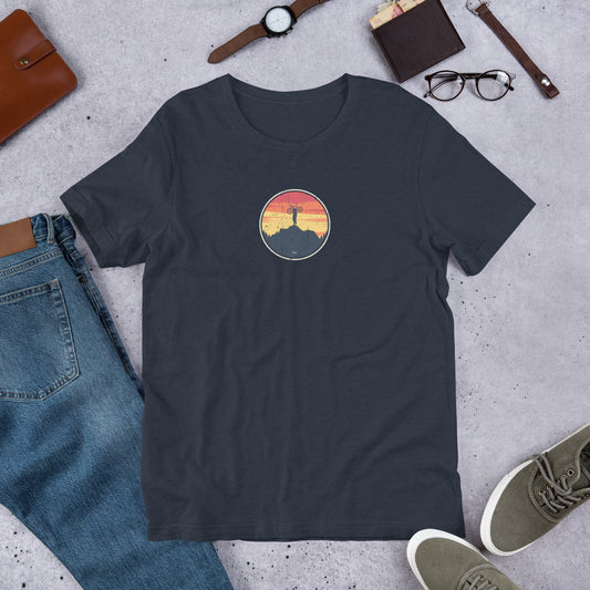 Black t-shirt with mountain bike graphic design on grey surface with jeans, shoes and accessories.