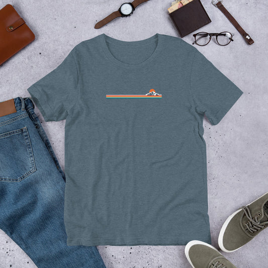Blue t-shirt with a graphic design on a concrete surface with jeans, shoes, and accessories.