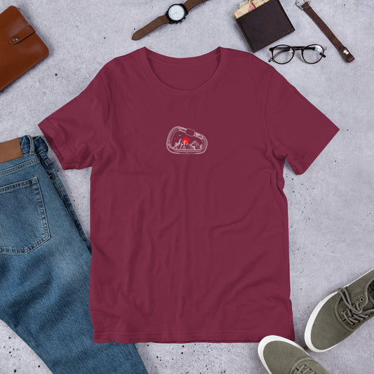 Maroon t-shirt with a graphic design on a gray surface with jeans, shoes, and accessories.