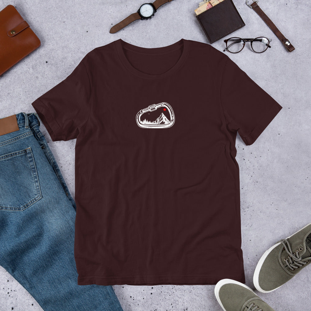 Brown t-shirt with a logo on a gray surface with jeans, shoes, and accessories.